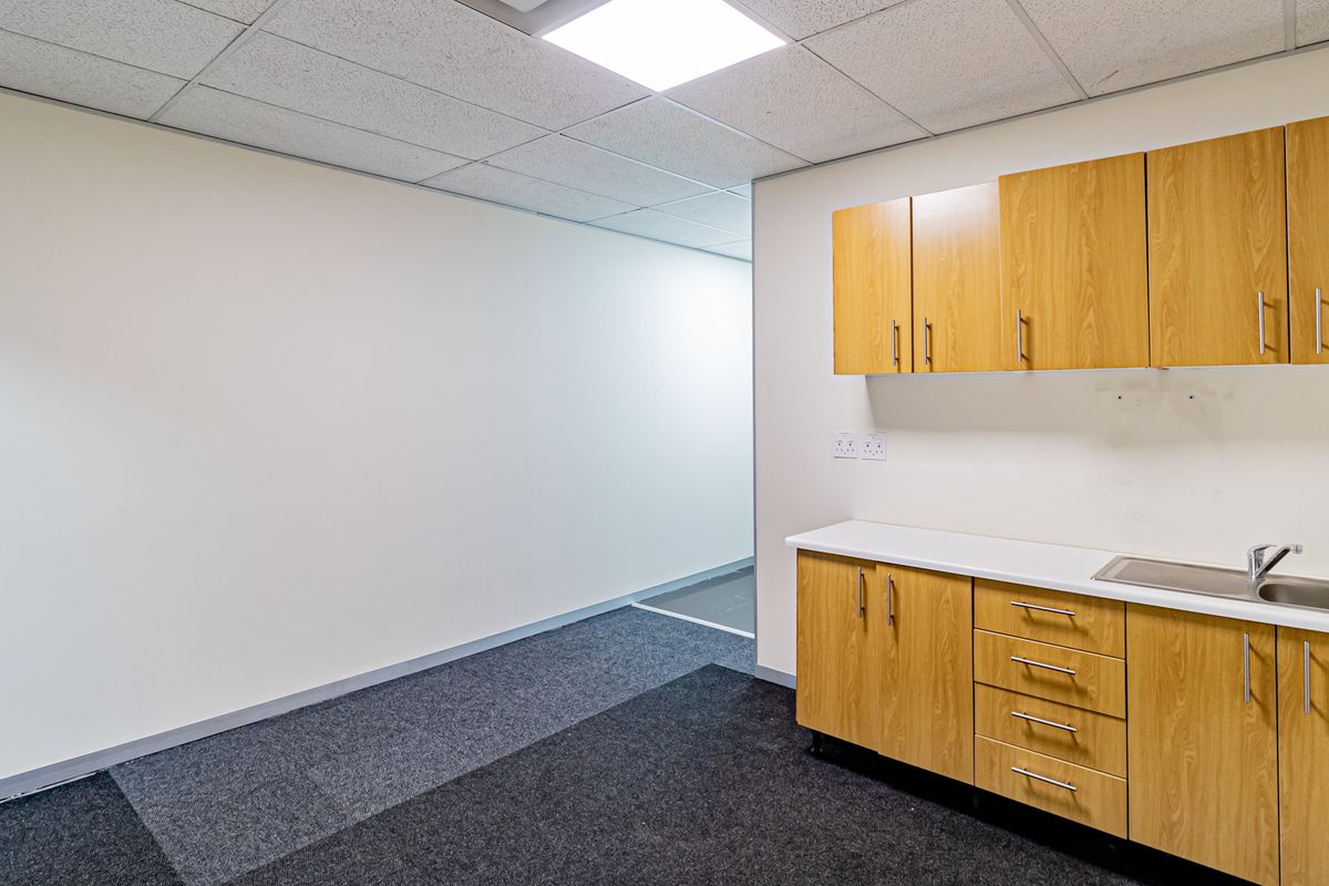 A functional office kitchenette featuring wood-grain cabinetry, a stainless steel sink, and a drop ceiling with integrated lighting.
