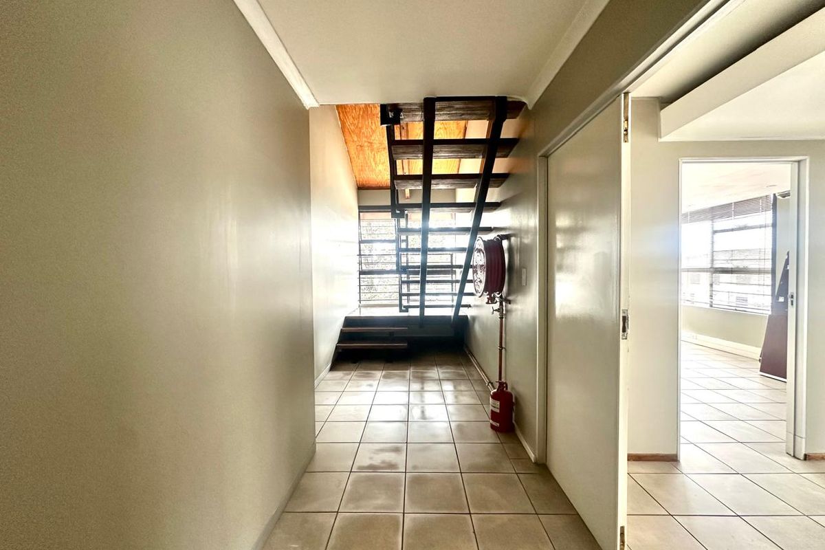 Commercial hallway featuring tiled flooring, an open-tread staircase, and a wall-mounted fire hose reel, leading to an adjacent office space.