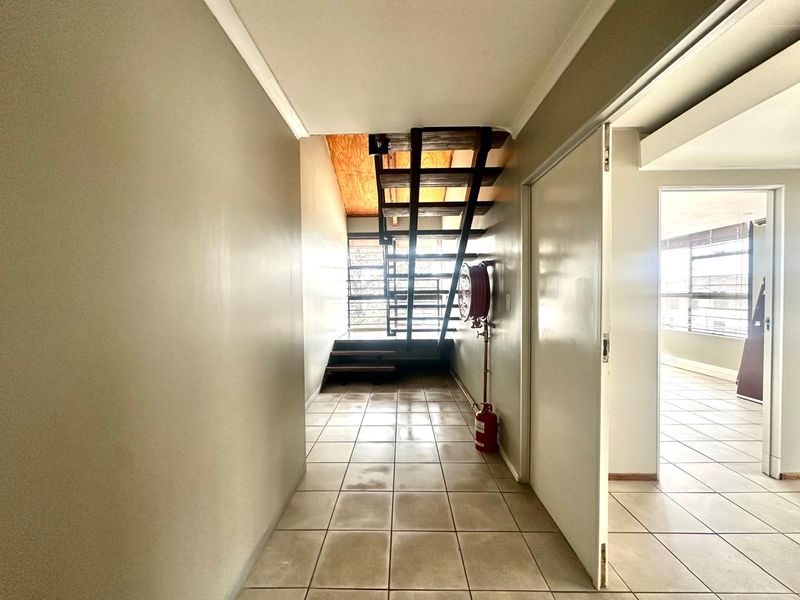 Commercial hallway featuring tiled flooring, an open-tread staircase, and a wall-mounted fire hose reel, leading to an adjacent office space.