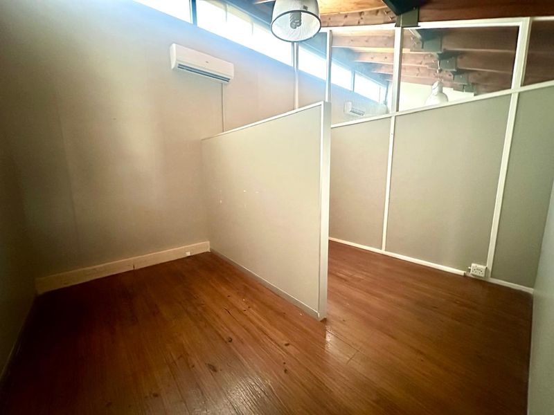 A partitioned office space featuring timber flooring, wall-mounted air conditioning units, and high-level clerestory windows providing natural light.