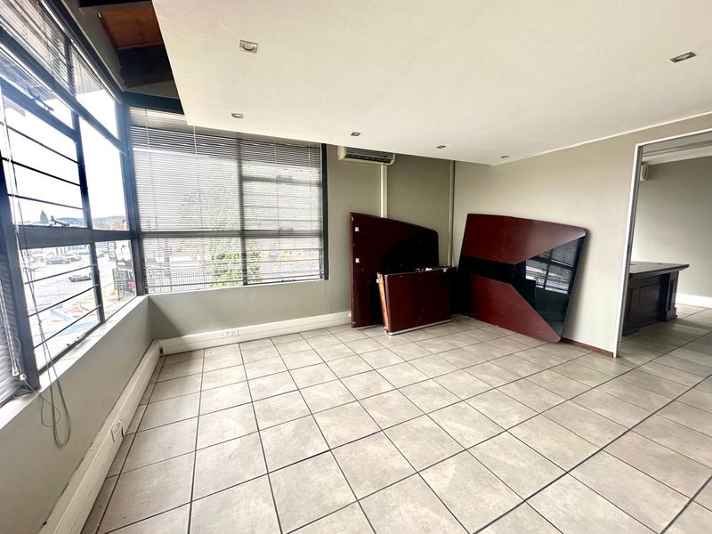A bright commercial office space featuring large windows, tiled flooring, recessed ceiling lighting, and a wall-mounted air conditioning unit.