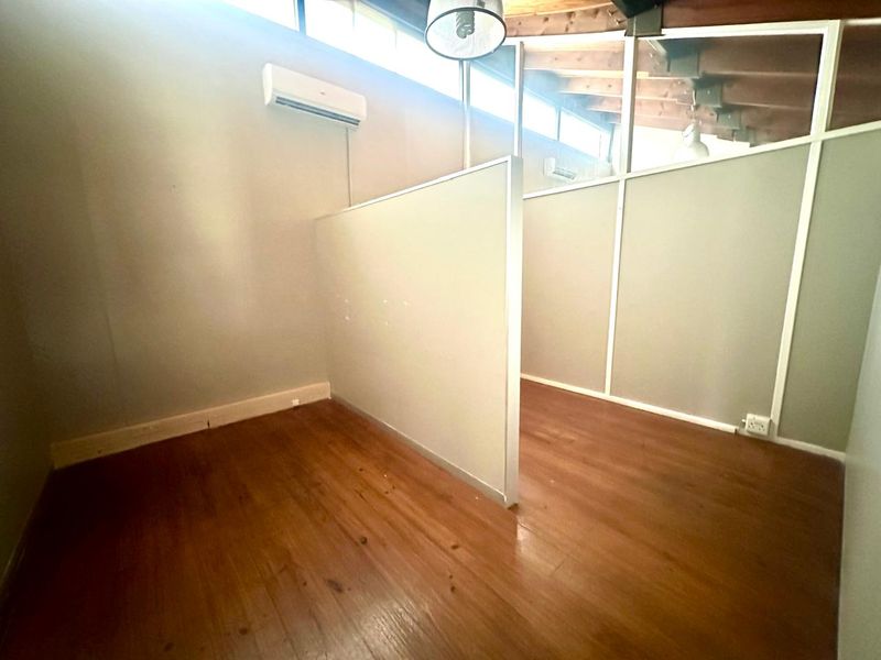 A partitioned office space featuring wood-look flooring, wall-mounted air conditioning units, and exposed timber ceiling beams with clerestory windows.