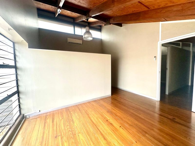 An open-plan office space featuring polished timber flooring, exposed wooden ceiling beams, clerestory windows, and a wall-mounted air conditioning unit.