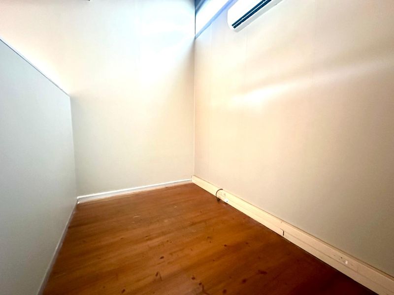 A compact, empty office space featuring timber flooring, a wall-mounted air conditioning unit, and neutral wall finishes.