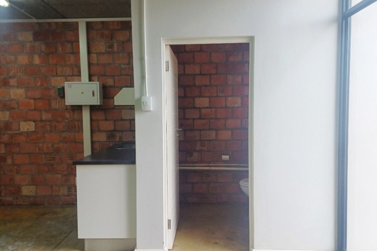 A functional office bathroom area featuring exposed brick walls, a built-in vanity, and basic utility fixtures in a utilitarian office setting.