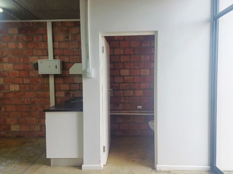 A functional office bathroom area featuring exposed brick walls, a built-in vanity, and basic utility fixtures in a utilitarian office setting.
