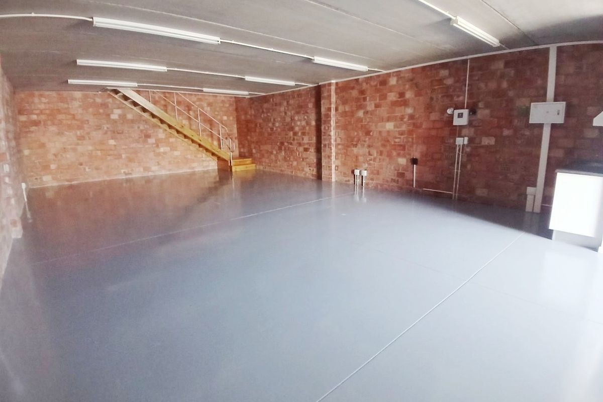 Spacious open-plan office area featuring exposed brick walls, durable epoxy flooring, and integrated staircase, offering a versatile workspace environment.