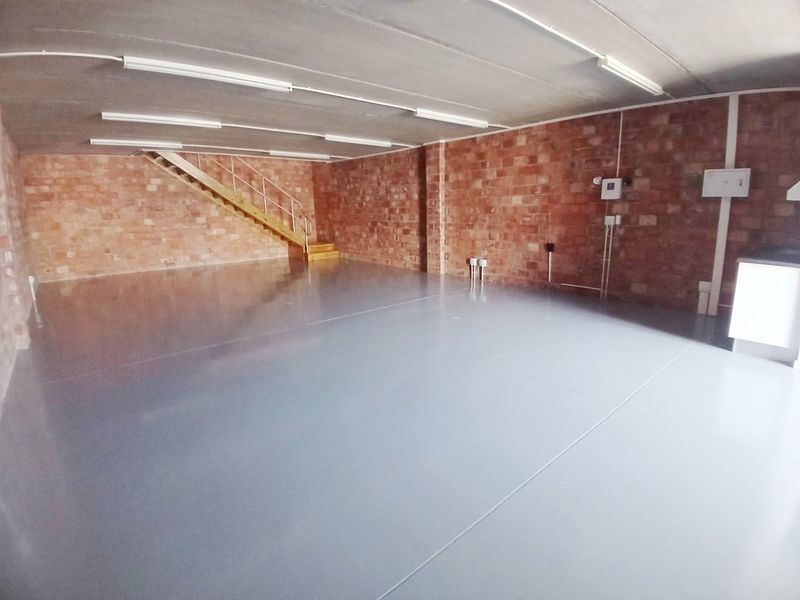Spacious open-plan office area featuring exposed brick walls, durable epoxy flooring, and integrated staircase, offering a versatile workspace environment.