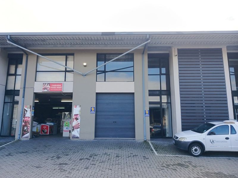 Front elevation of a commercial office or retail unit featuring a roller shutter door, large glass windows, and paved parking area.