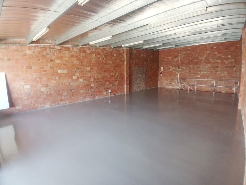Spacious open-plan office area featuring exposed brick walls, polished epoxy flooring, and an industrial-style exposed steel ceiling structure.