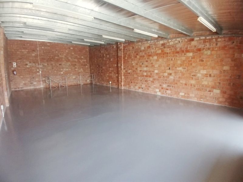 Spacious open-plan office area featuring exposed brick walls, polished epoxy flooring, and industrial-style exposed steel ceiling beams with integrated lighting.