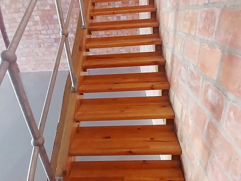 A functional timber staircase featuring a metal balustrade and an exposed brick feature wall, providing access between levels in this office space.