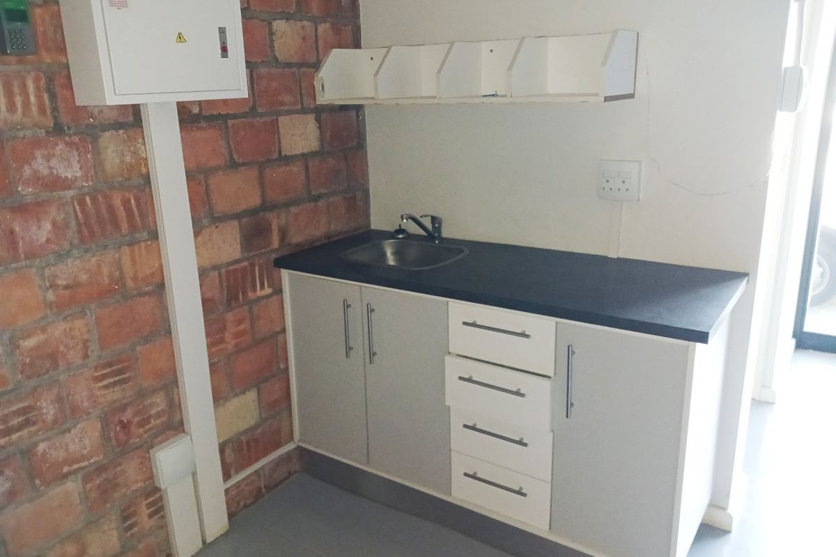 A functional utility kitchenette area featuring built-in cabinetry, a sink, and an exposed brick feature wall within an office environment.
