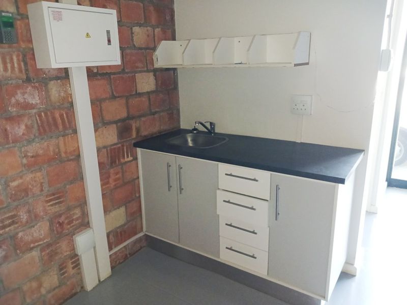 A functional utility kitchenette area featuring built-in cabinetry, a sink, and an exposed brick feature wall within an office environment.