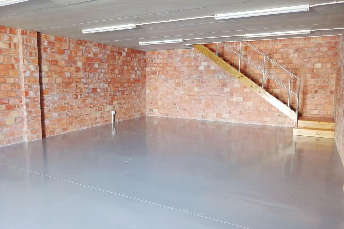 Spacious open-plan office area featuring exposed brick walls, polished epoxy flooring, and a timber staircase leading to an upper level.