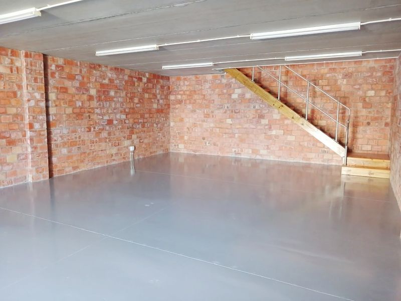 Spacious open-plan office area featuring exposed brick walls, polished epoxy flooring, and a timber staircase leading to an upper level.