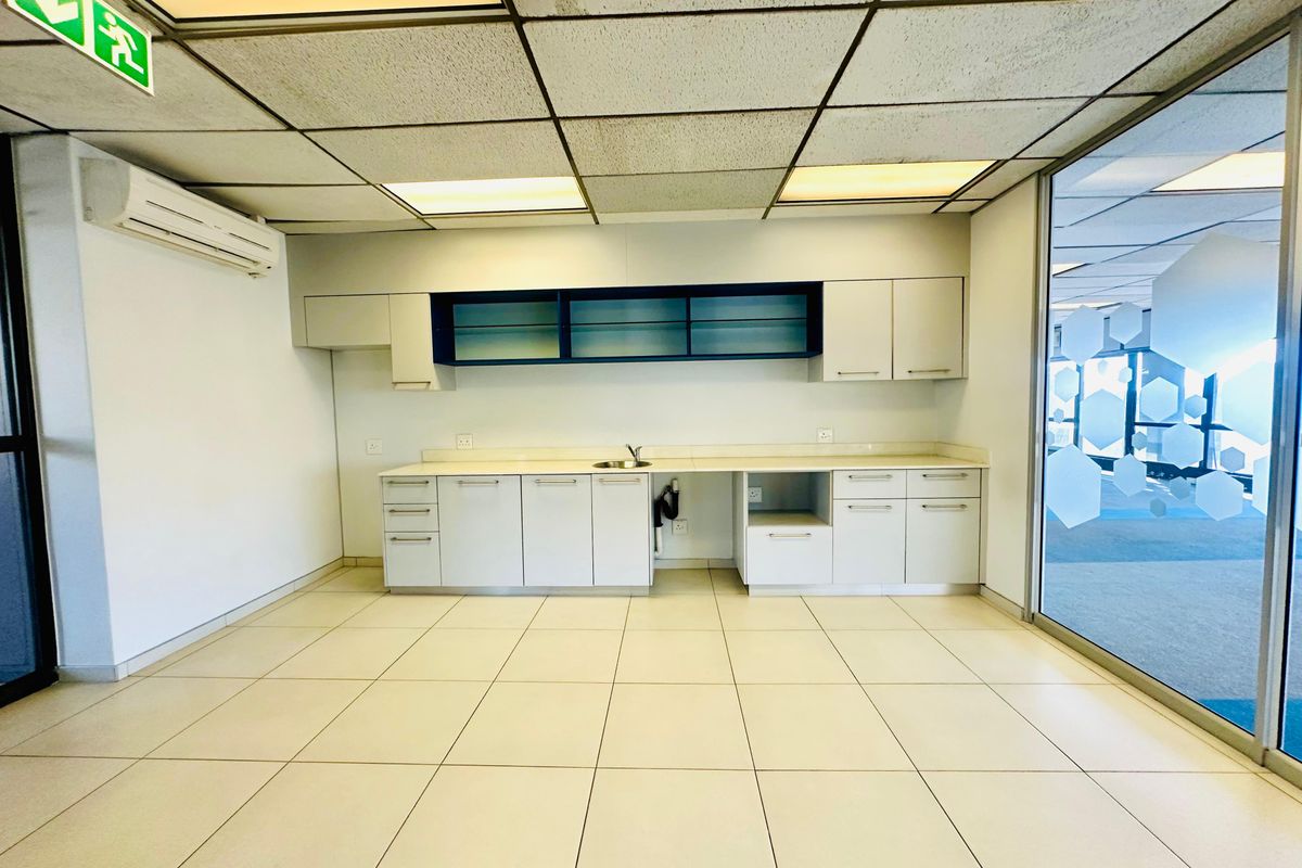 A functional commercial kitchenette featuring built-in cabinetry, a stainless steel sink, and recessed lighting, suitable for office or workspace utility.