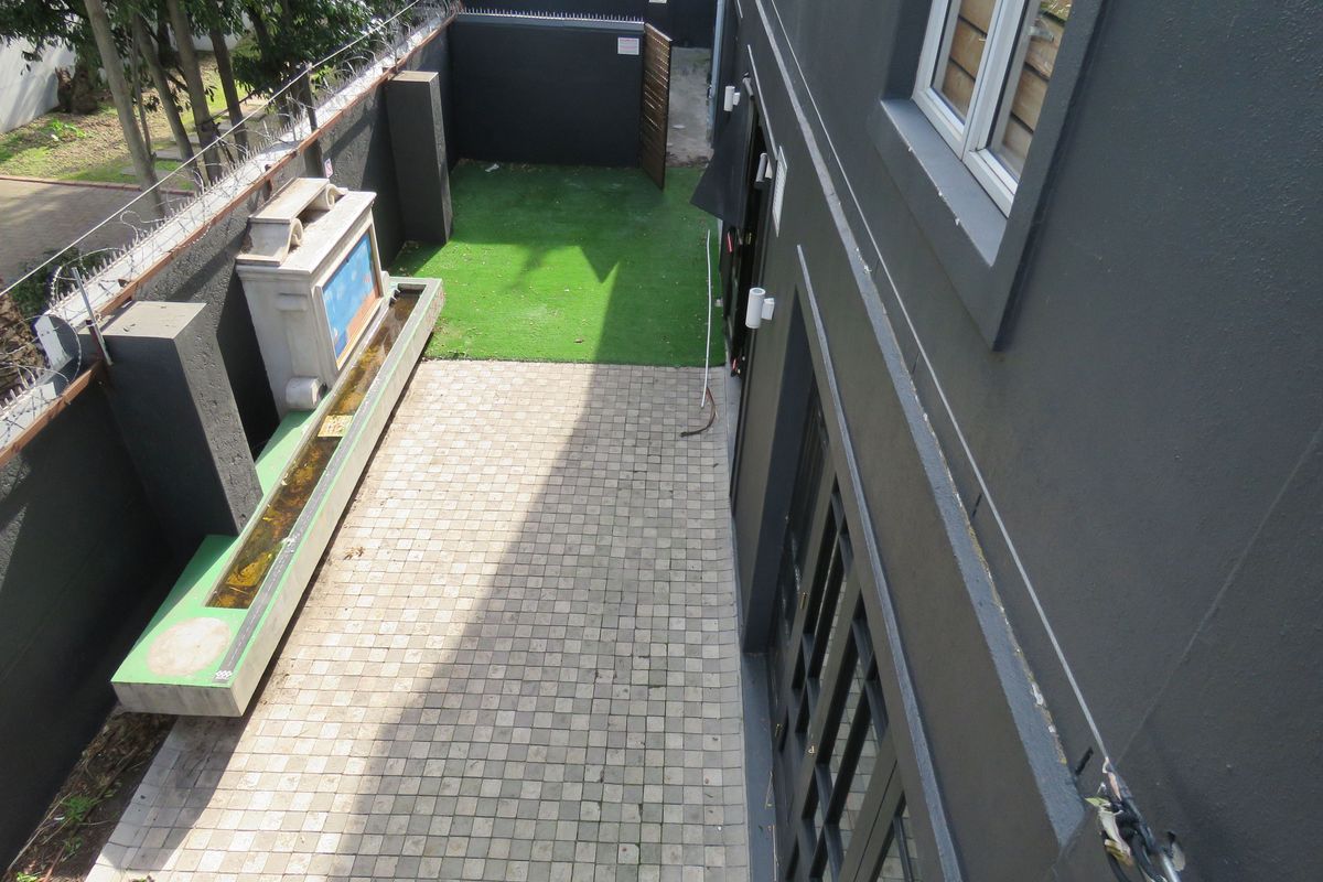 An elevated view of a rear courtyard featuring paved areas, artificial lawn, a built-in water feature, and secure perimeter walling.
