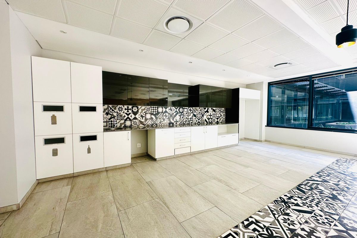 Modern office kitchenette featuring high-gloss cabinetry, patterned tile backsplash, integrated storage, and large windows providing ample natural light.