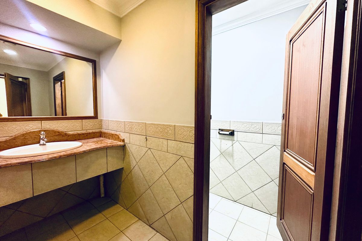 A functional office restroom featuring a built-in vanity with a marble-look countertop, ceramic wall tiling, and a wooden door entrance.
