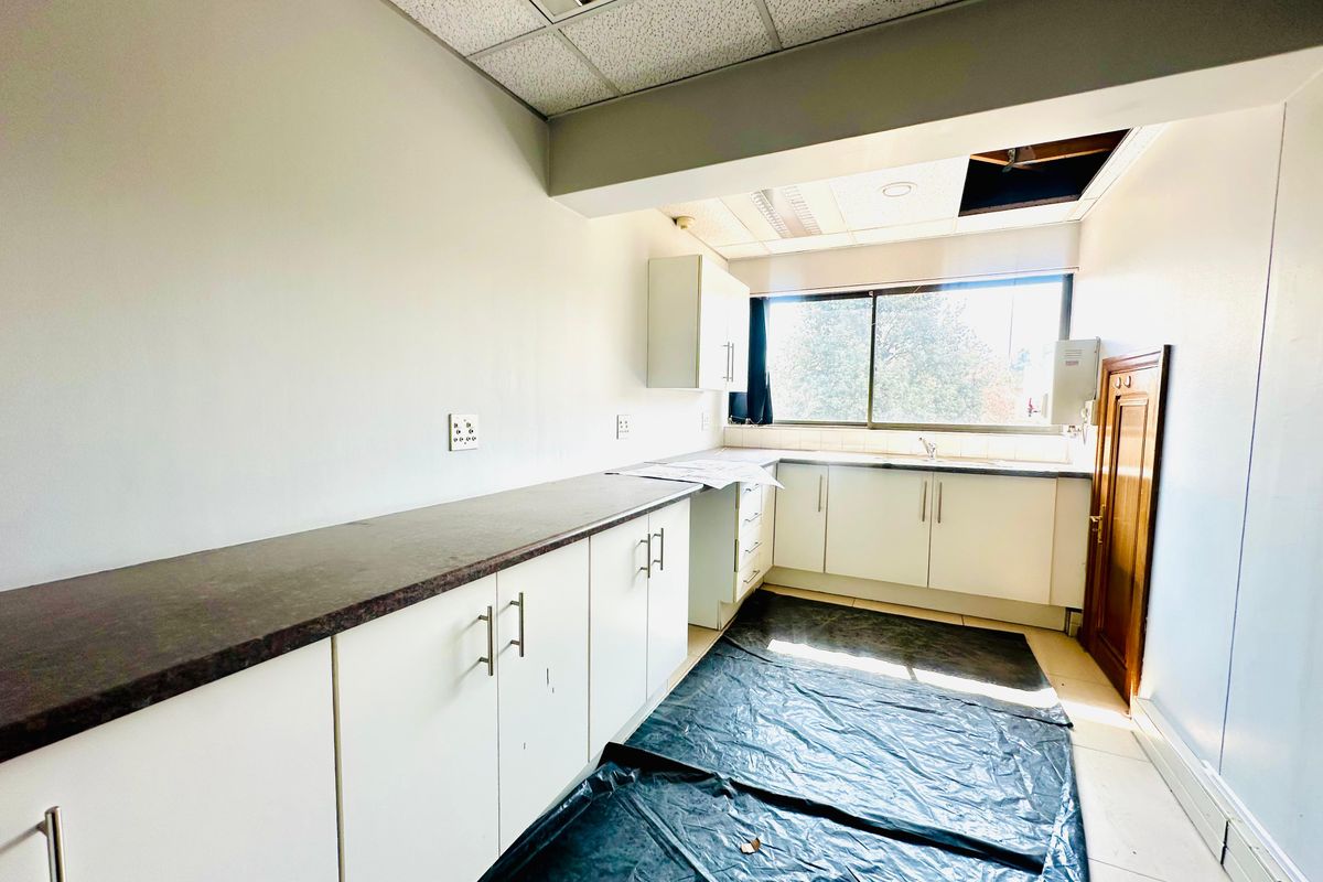 A functional office kitchenette featuring white cabinetry, dark laminate countertops, and a stainless steel sink, currently undergoing maintenance or minor repairs.