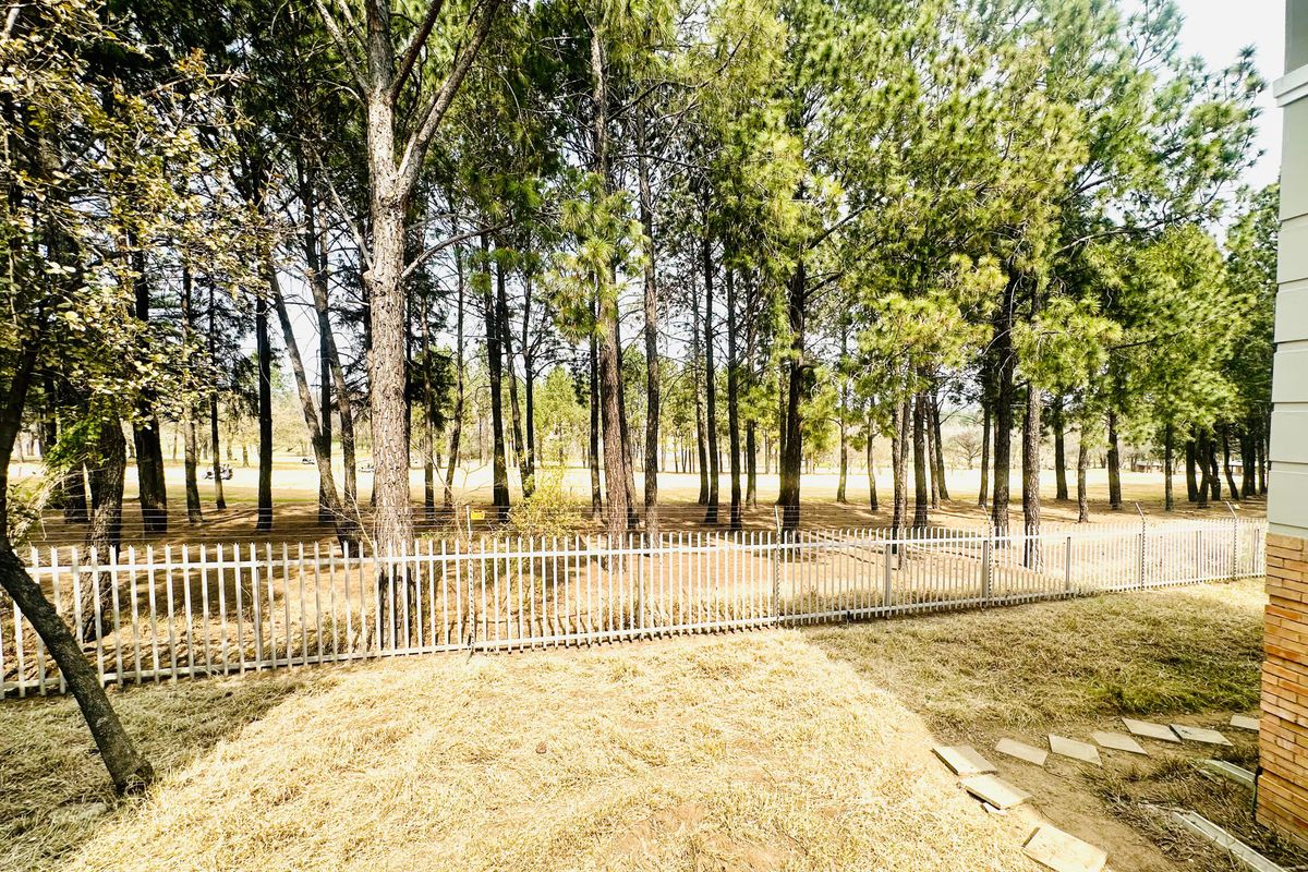 A view of the rear garden area featuring a metal security fence and mature pine trees, overlooking a golf course.