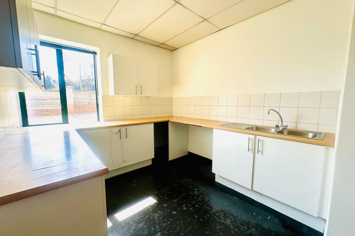 A functional office kitchenette featuring white cabinetry, a stainless steel sink, tiled splashbacks, and a drop ceiling.
