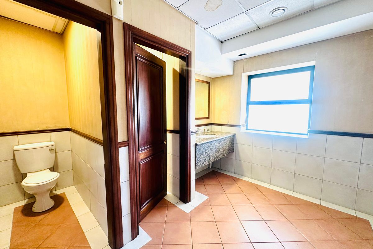 A functional office restroom featuring a private toilet cubicle, a granite-topped vanity with a sink, and tiled flooring.