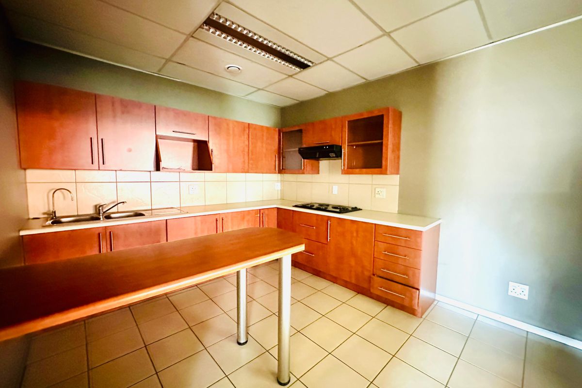 A functional office kitchenette featuring wooden cabinetry, a built-in hob, extractor fan, and a stainless steel sink with tiled splashbacks.
