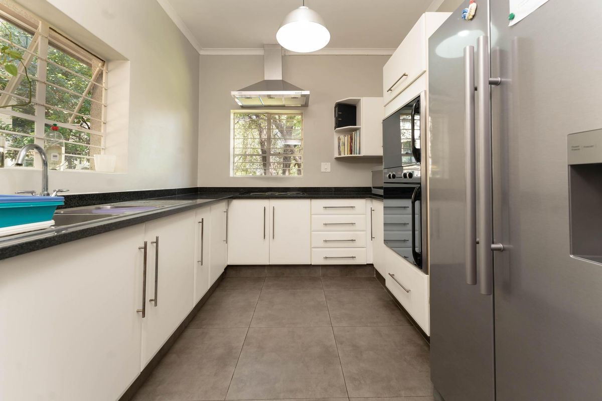 Modern kitchen featuring white cabinetry, dark granite countertops, stainless steel extractor fan, built-in oven, and tiled flooring.