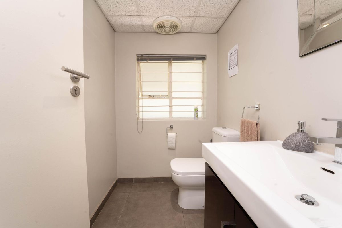 A functional office restroom featuring a modern vanity, toilet, tiled flooring, and a drop ceiling with integrated ventilation.