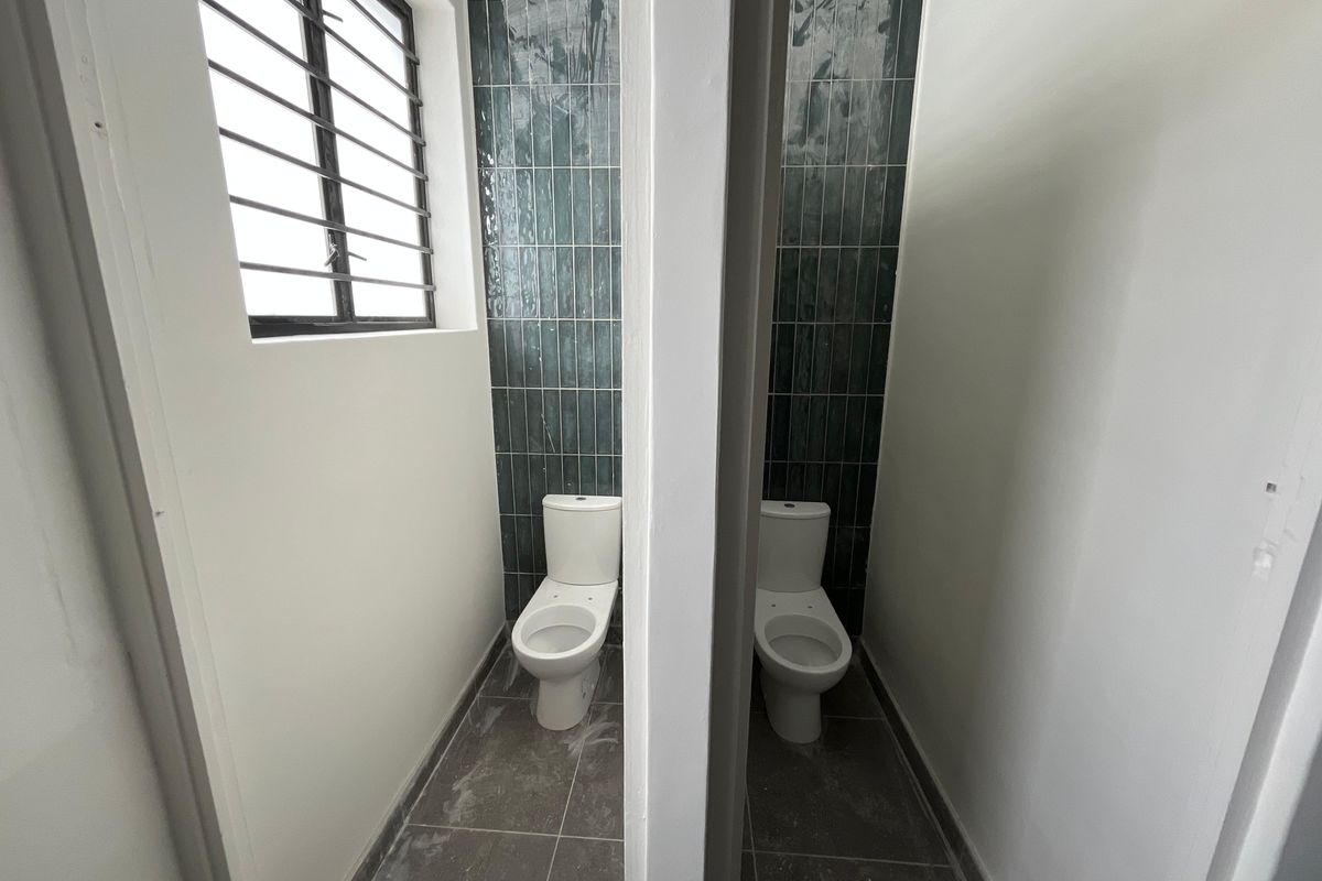 Two adjacent restroom stalls featuring modern dark vertical wall tiles, grey floor tiles, and white ceramic toilets with security bars on the window.