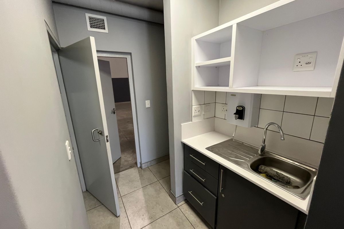 A compact kitchenette area featuring a stainless steel sink, built-in cabinetry, and tiled flooring, providing functional utility space within the industrial unit.