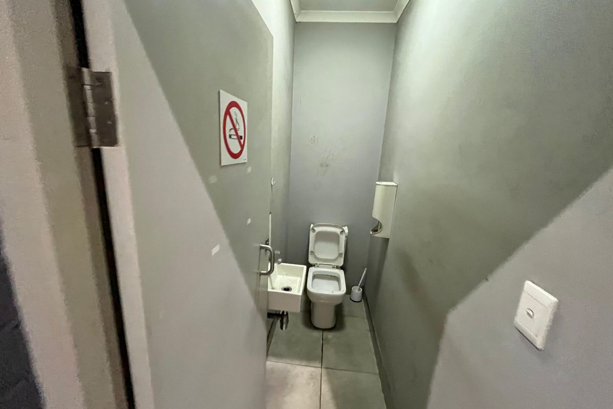 A compact industrial-style restroom featuring a wall-mounted basin and a standard toilet, finished with grey painted walls and tiled flooring.