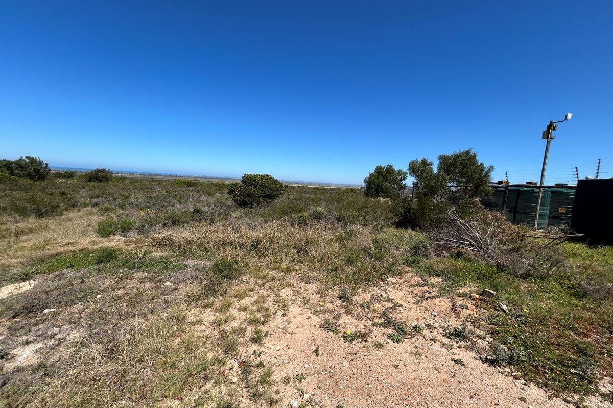 A wide-angle view of the vacant commercial land, featuring natural vegetation, clear horizon, and existing water storage tanks on the property boundary.