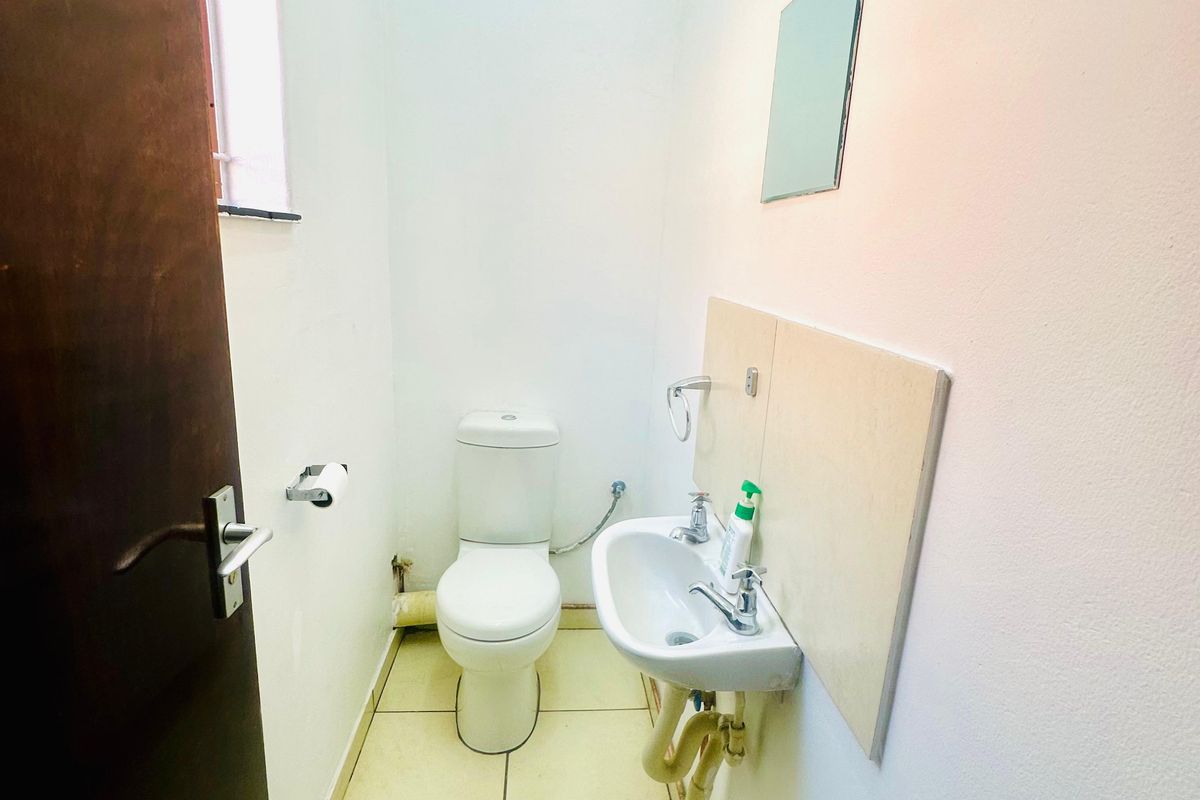 A compact commercial restroom featuring a standard toilet, wall-mounted basin with exposed plumbing, and tiled flooring.
