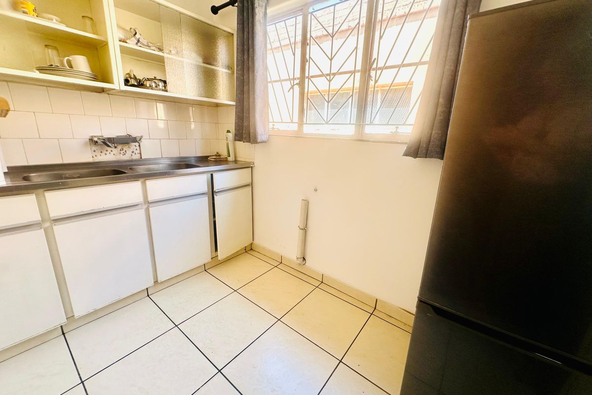 A functional kitchen area featuring built-in cabinetry, a stainless steel sink, tiled flooring, and security bars on the window.