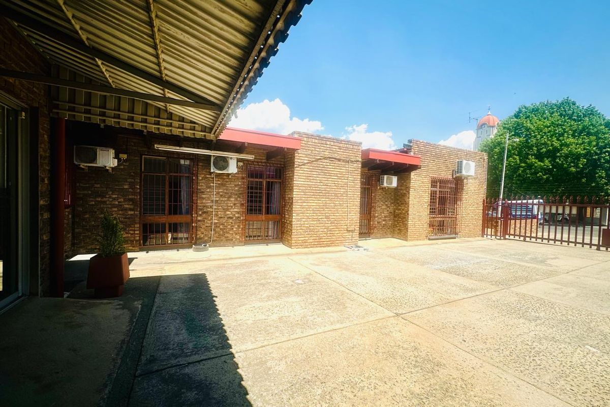 Exterior view of a commercial property featuring a brick facade, covered patio area, and paved courtyard with multiple wall-mounted air conditioning units.