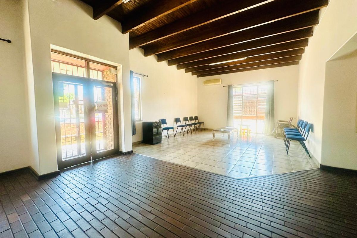 Spacious commercial waiting area featuring exposed timber beam ceilings, tiled flooring, and large windows with security bars.