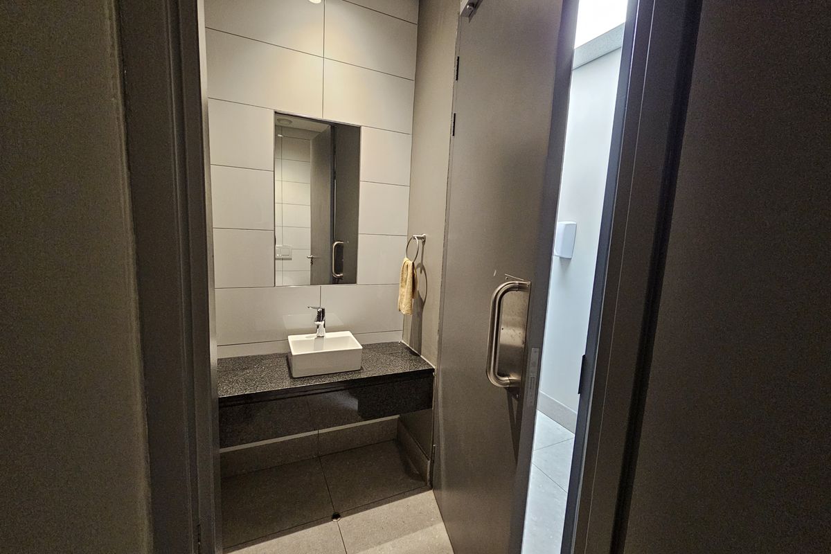 A modern office restroom featuring a sleek vanity with a vessel sink, polished stone countertop, and large format wall tiles.