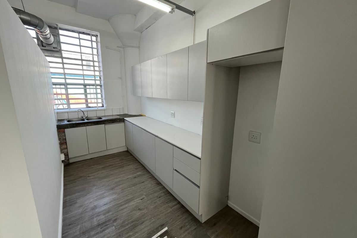 A functional kitchenette featuring modern grey cabinetry, stone-look countertops, a double sink, and industrial-style window with security bars.