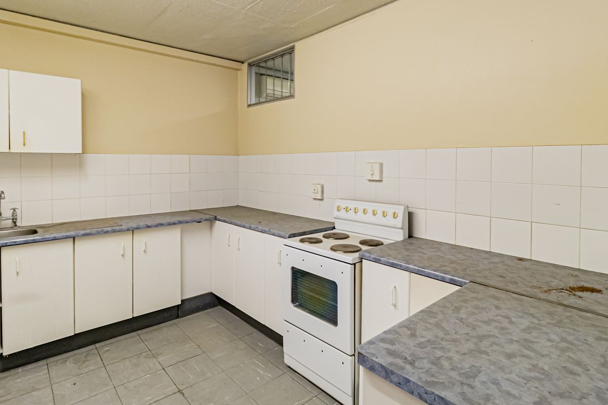A functional office kitchenette featuring white cabinetry, tiled splashbacks, a built-in sink, and a freestanding electric stove.