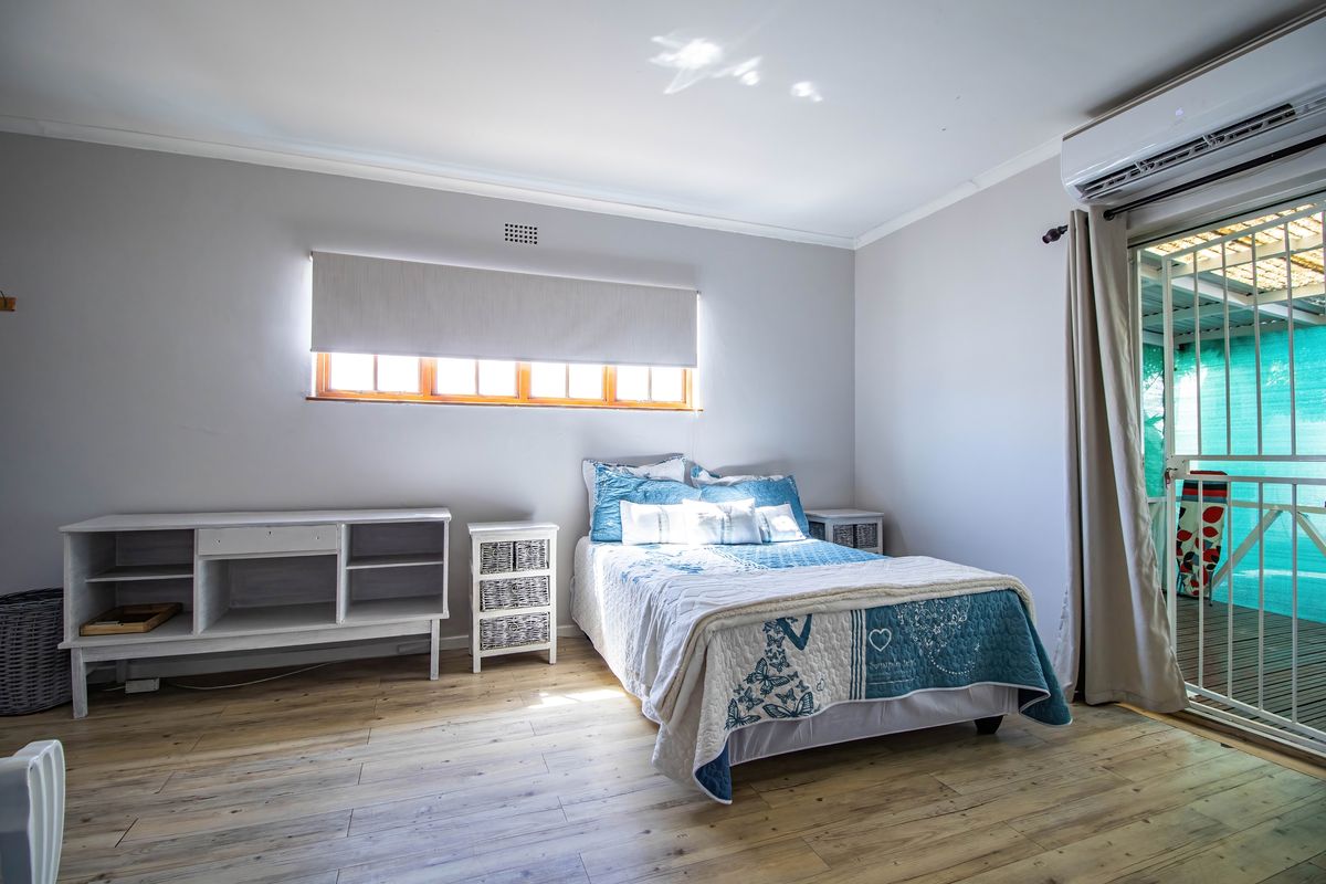 A bright bedroom featuring light wood-look flooring, a wall-mounted air conditioning unit, and a sliding glass door providing access to an outdoor area.