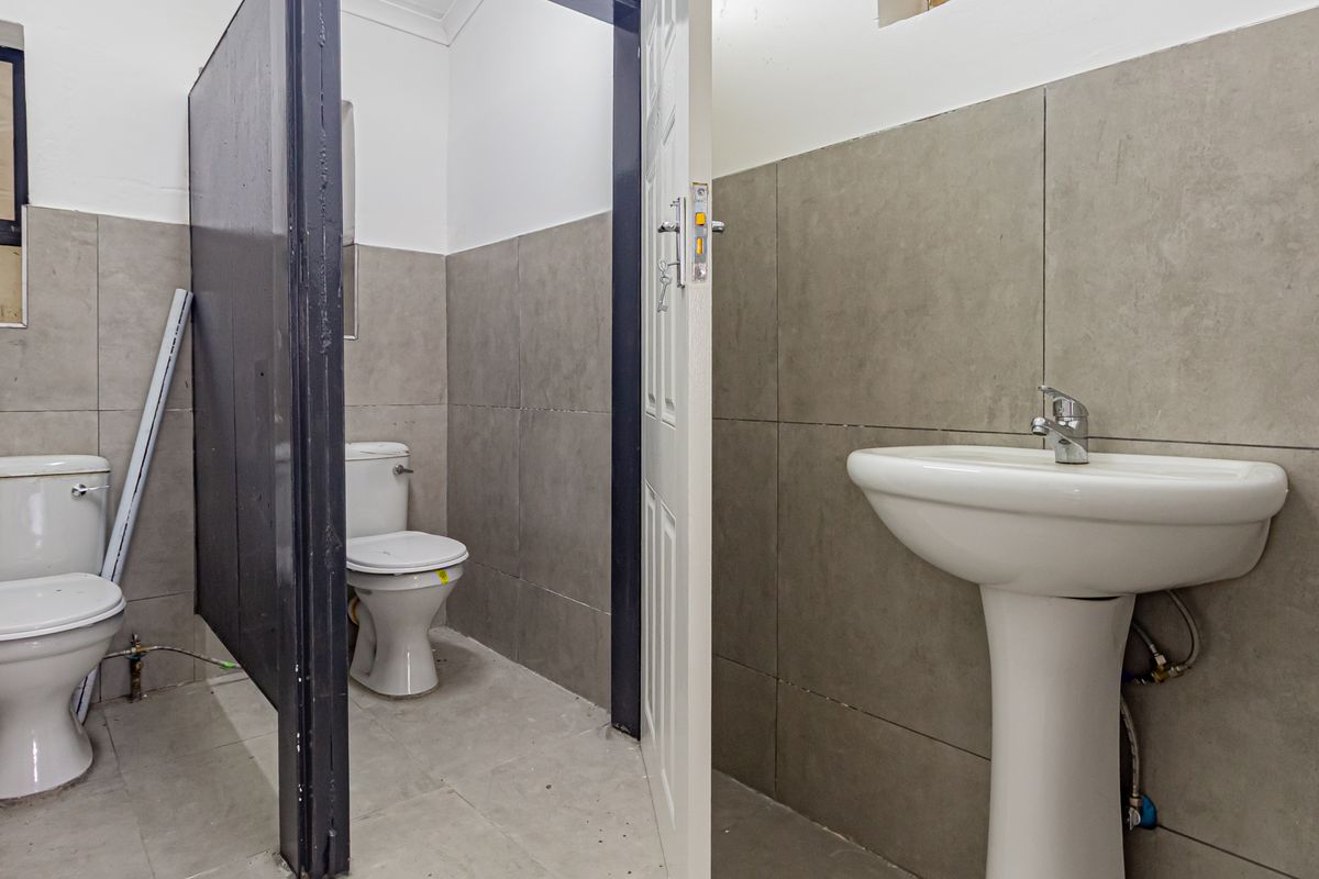 A functional office restroom featuring a pedestal basin and two separate toilet cubicles with grey wall tiling.