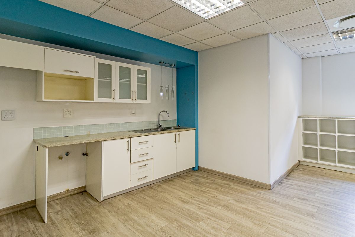 A functional office kitchenette featuring white cabinetry, granite countertops, a stainless steel sink, and wood-look flooring with a drop ceiling.