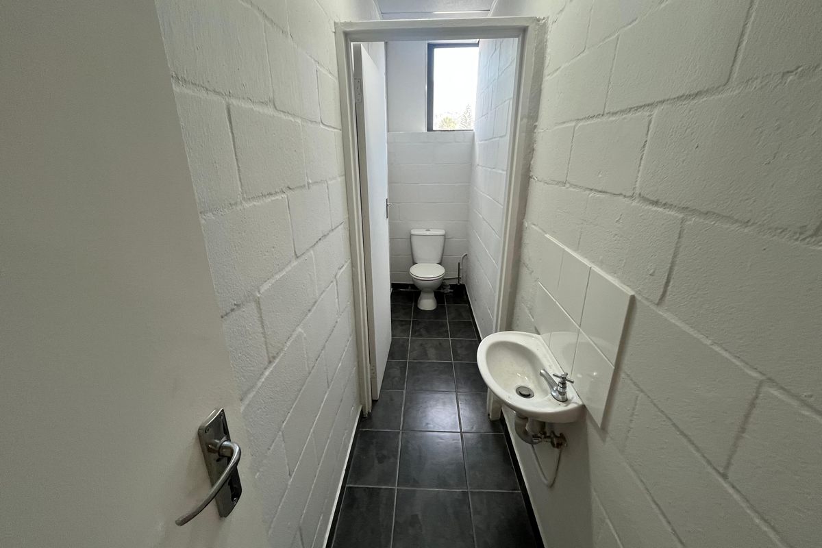 A functional industrial-style restroom featuring a wall-mounted basin, tiled flooring, and painted blockwork walls.