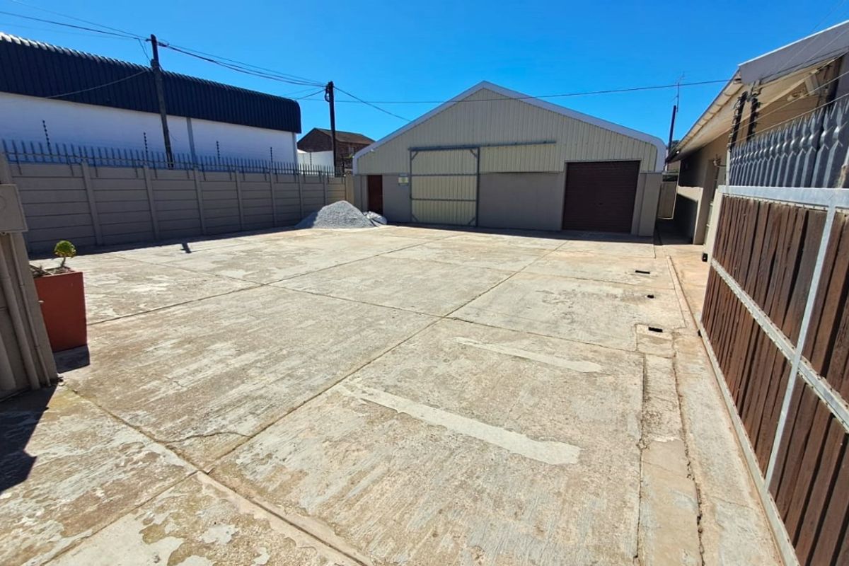 A spacious commercial yard area featuring concrete paving, perimeter walling with security fencing, and access to a large warehouse-style structure.