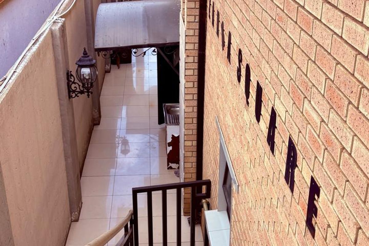 An exterior view of a commercial property featuring a tiled staircase leading down to a narrow paved walkway with wall-mounted lighting and brick facade.