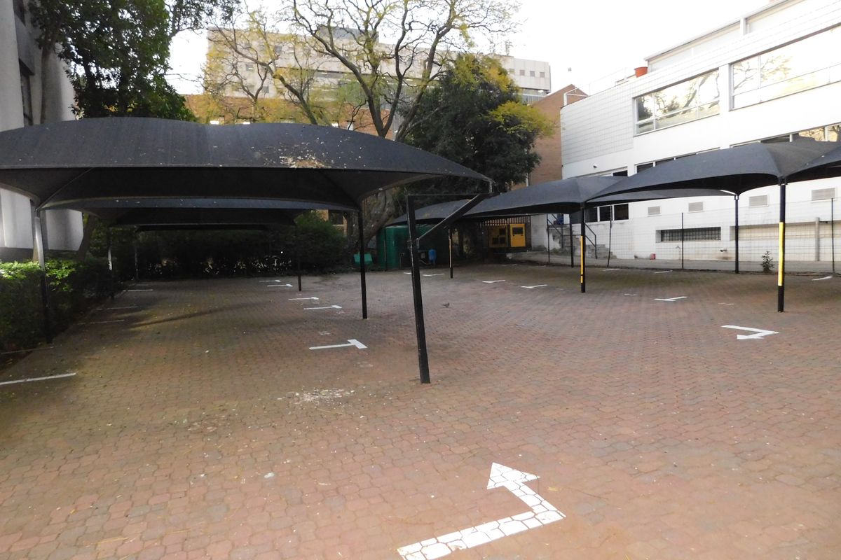 Outdoor parking area featuring paved ground and multiple black shade cloth structures for vehicle protection.
