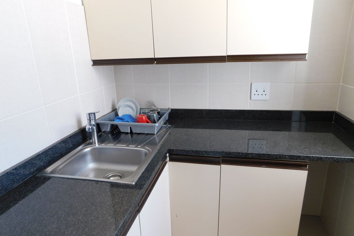 A compact kitchen area featuring dark granite countertops, light-toned cabinetry, a stainless steel sink, and tiled splashbacks.